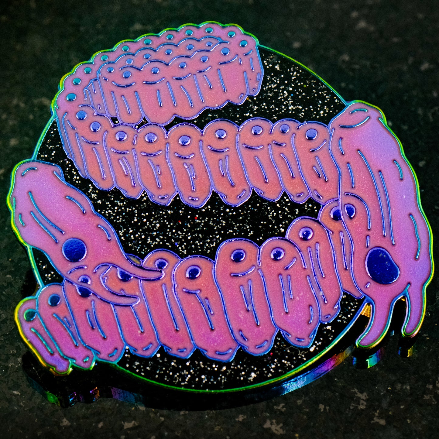 A photo of a soft enamel pin featuring Salps on a glittery black background with iridescent metal and bright magenta enamel. Rare