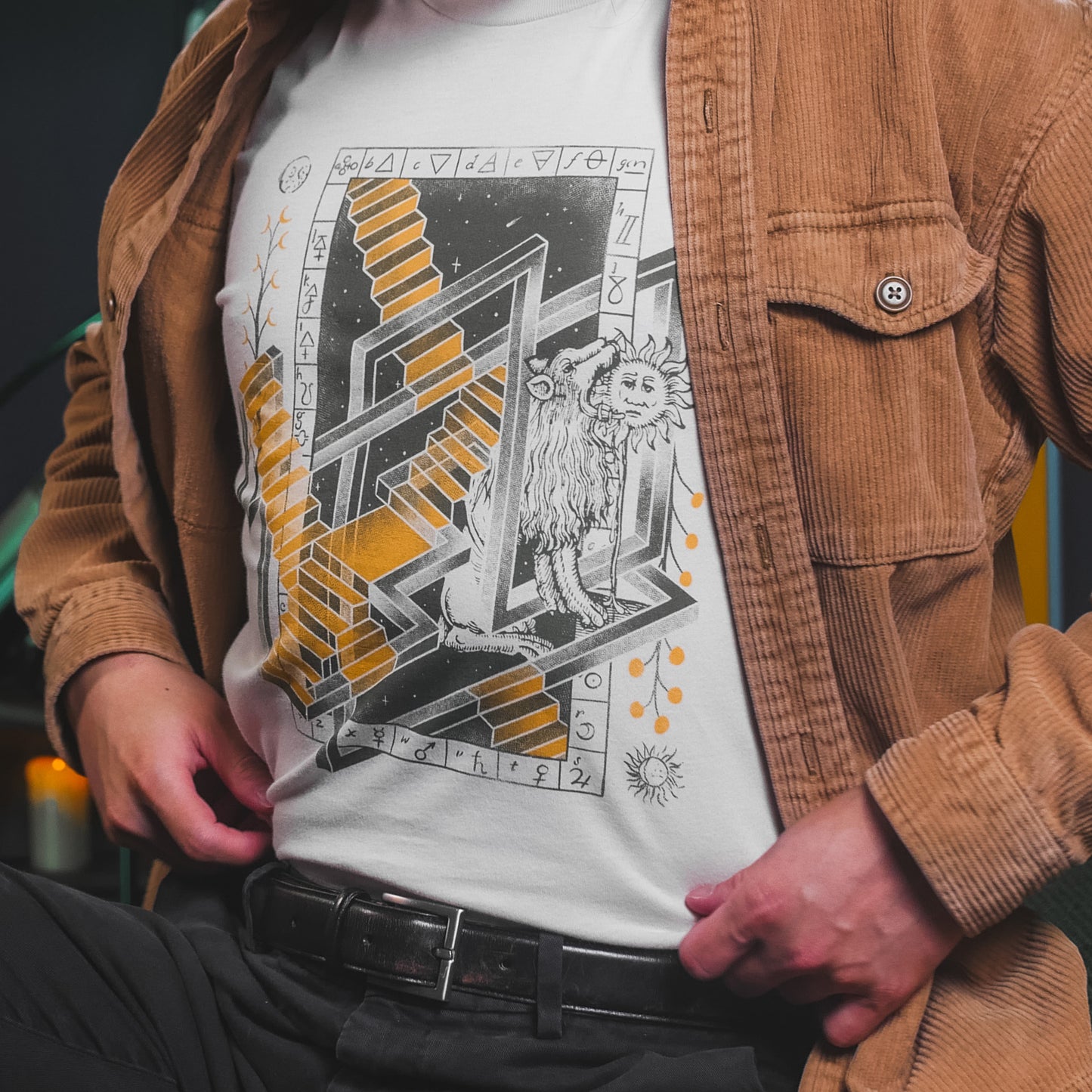 A closeup of someone wearing an off-white t-shirt with a graphic in green and yellow featuring various alchemical symbols. From SciShow.