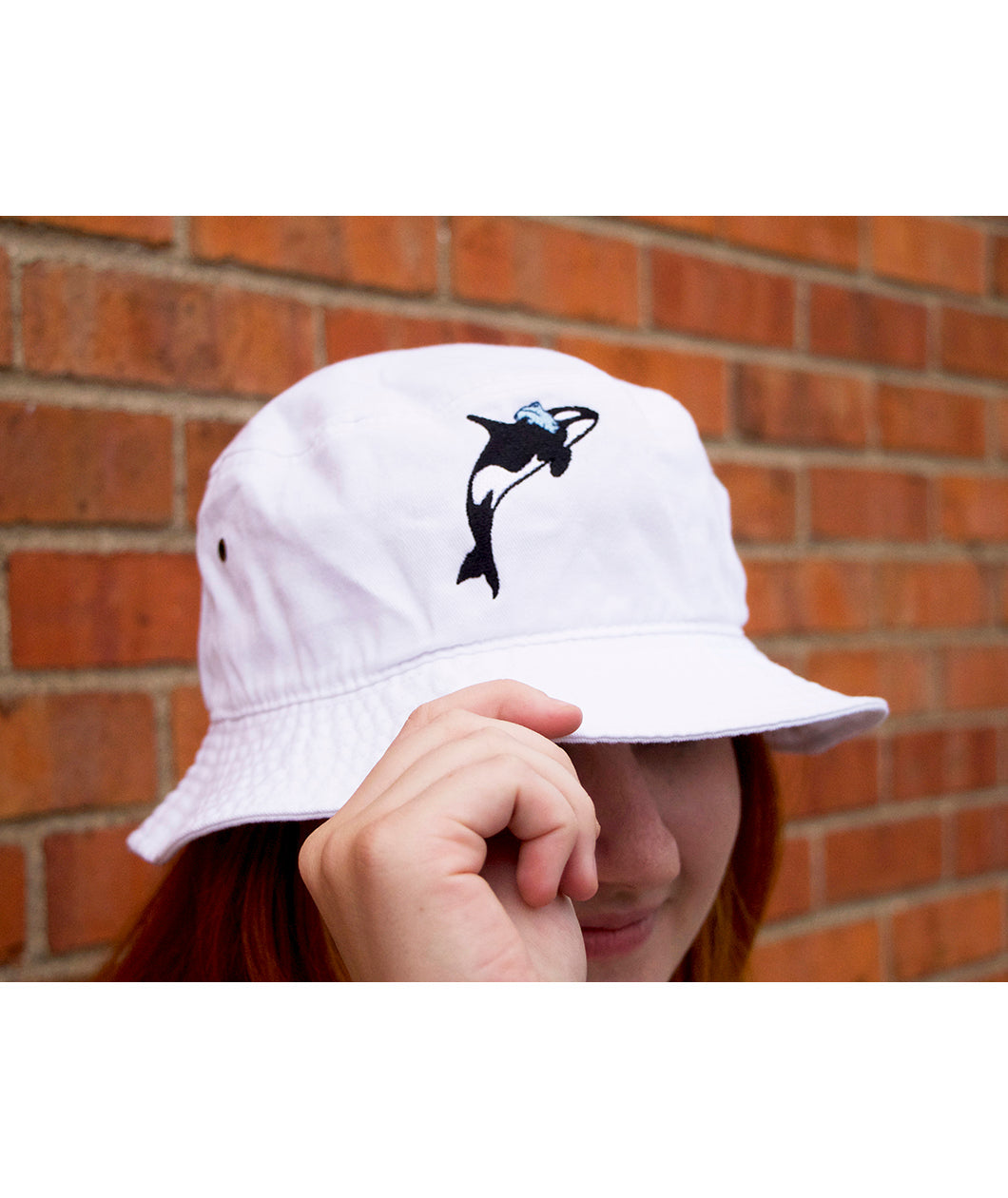A person's head wearing a white bucket hat with a orca whale on the front. From Scishow.