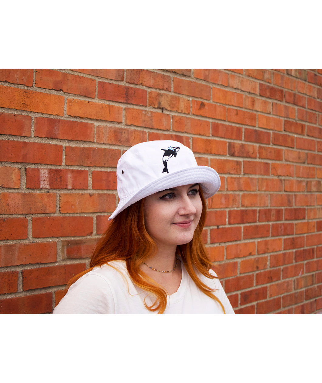 A person's head wearing a white bucket hat with a orca whale on the front. From Scishow.