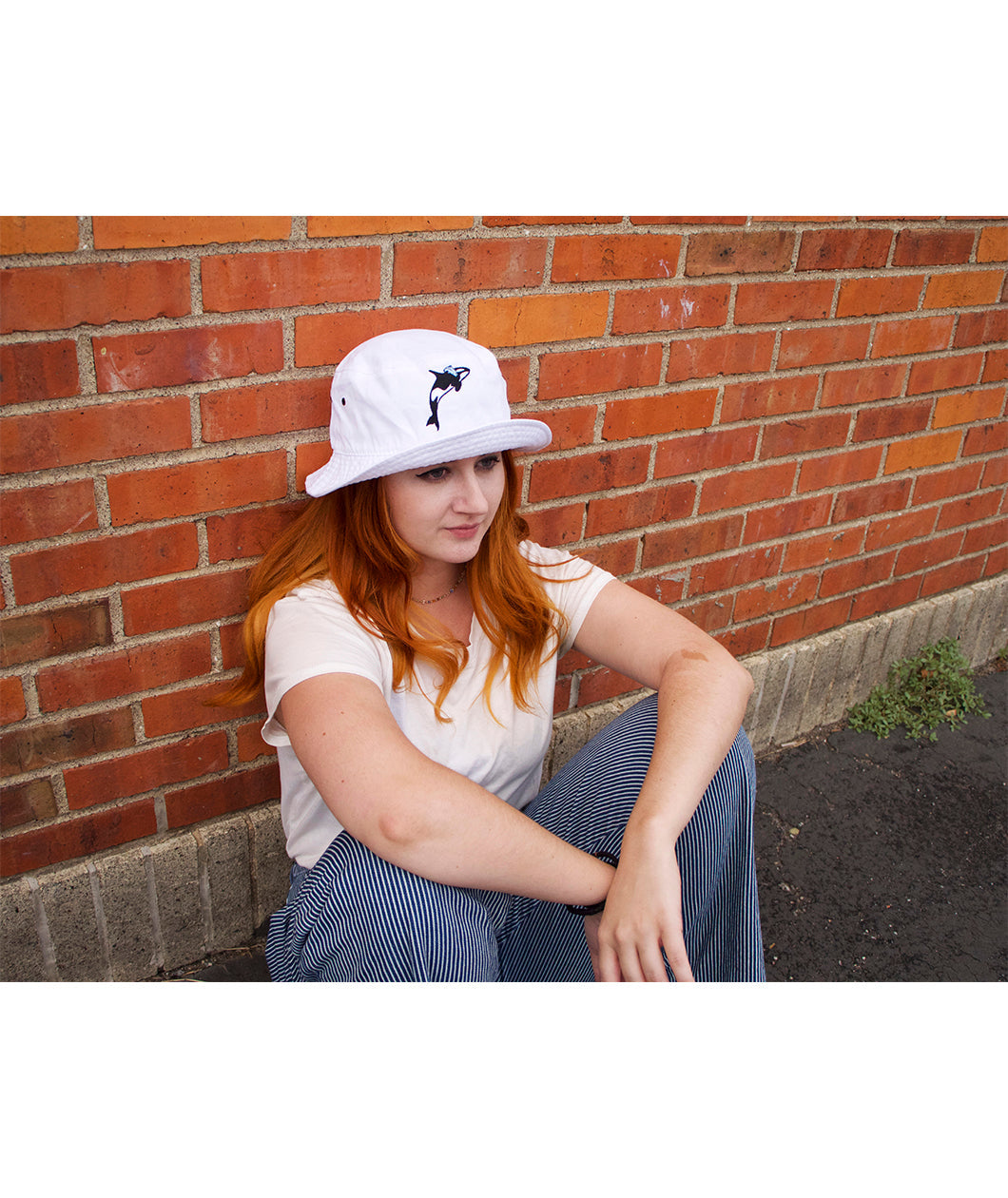 A person's head wearing a white bucket hat with a orca whale on the front. From Scishow.