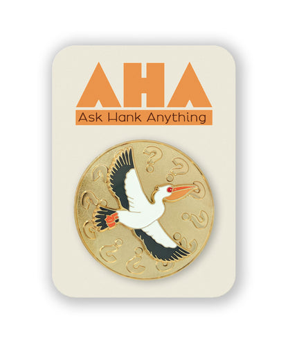 An image of a round gold pin on a cream colored backer card. The pin features a circle of question marks and a pelican flying with its wings spread wide as a spinner in the middle. The backer card has the Ask Hank Anything logo.