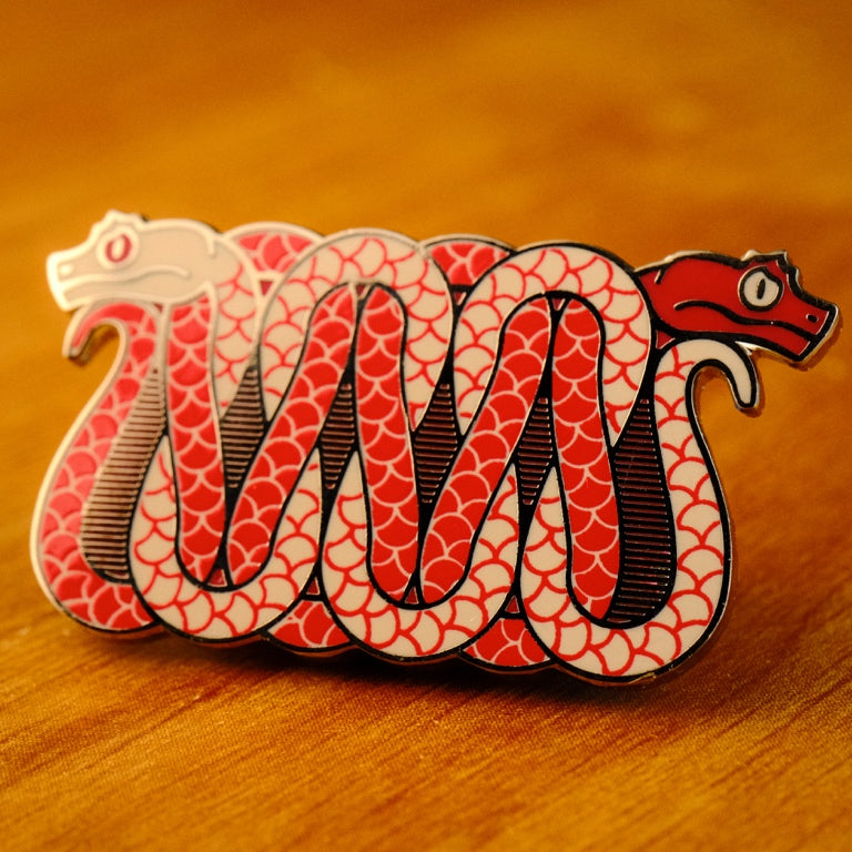 A photo of a soft enamel pin featuring eyelash vipers in red and cream enamel with black metal plating. Uncommon
