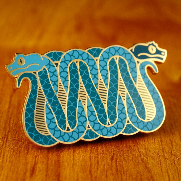 A photo of a soft enamel pin featuring eyelash vipers in blue and teal enamel with gold metal plating. Rare