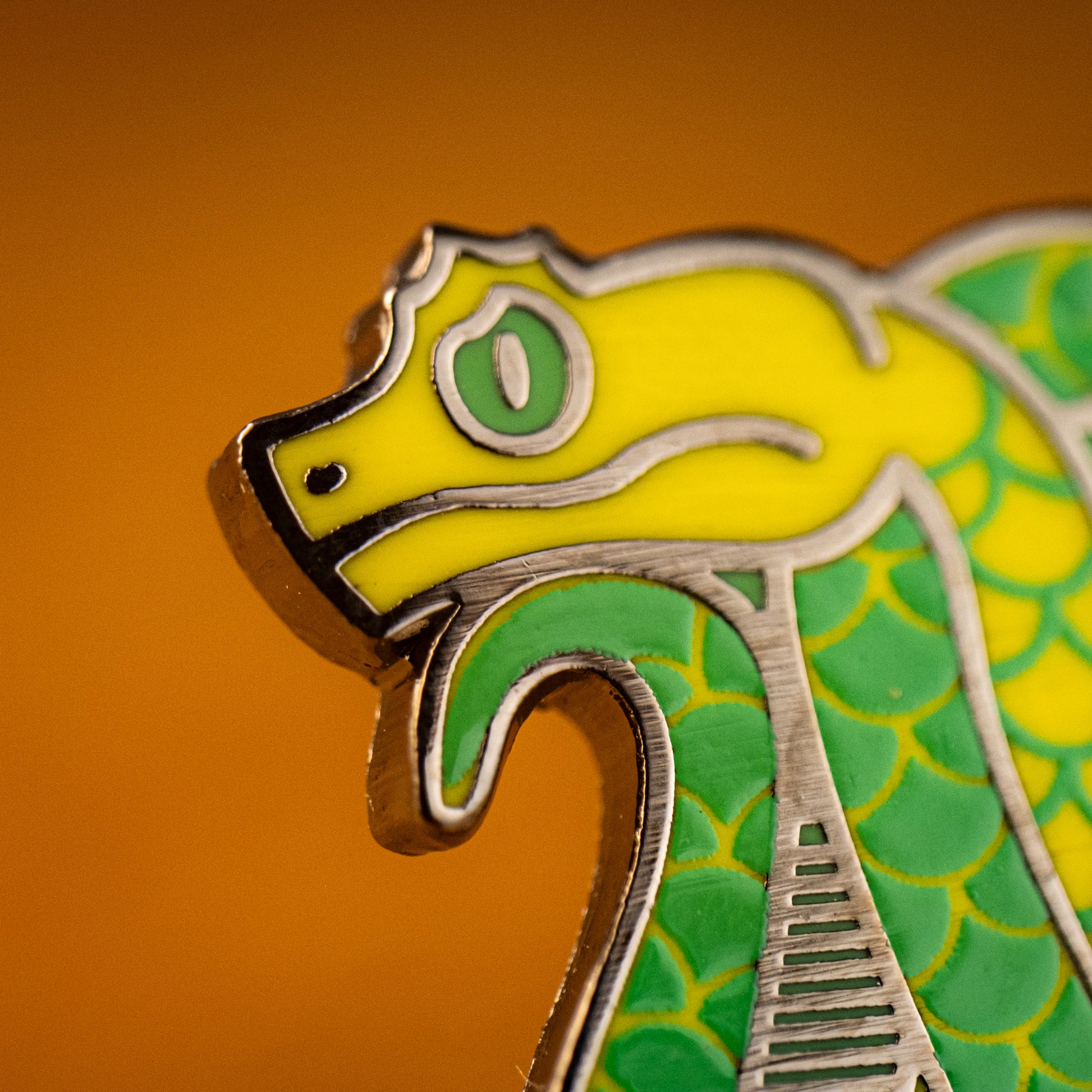 A close up photo of a soft enamel pin featuring eyelash vipers in green and yellow enamel with black metal plating, showcasing the metal plating as the iris and around the eye.