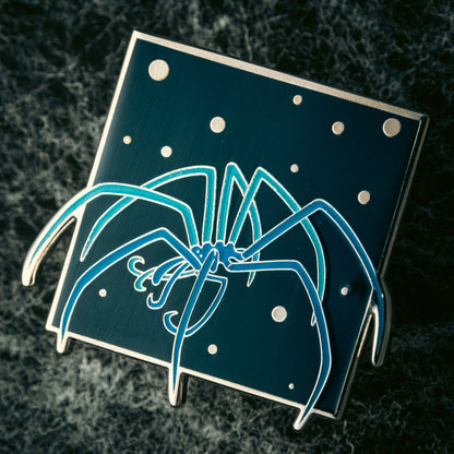 A photo of a soft enamel pin featuring a Sea Spider with blue enamel coloring and silver plating. Uncommon
