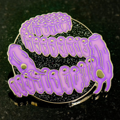 A photo of a soft enamel pin featuring Salps on a glittery black background with gold metal and light purple enamel. Uncommon