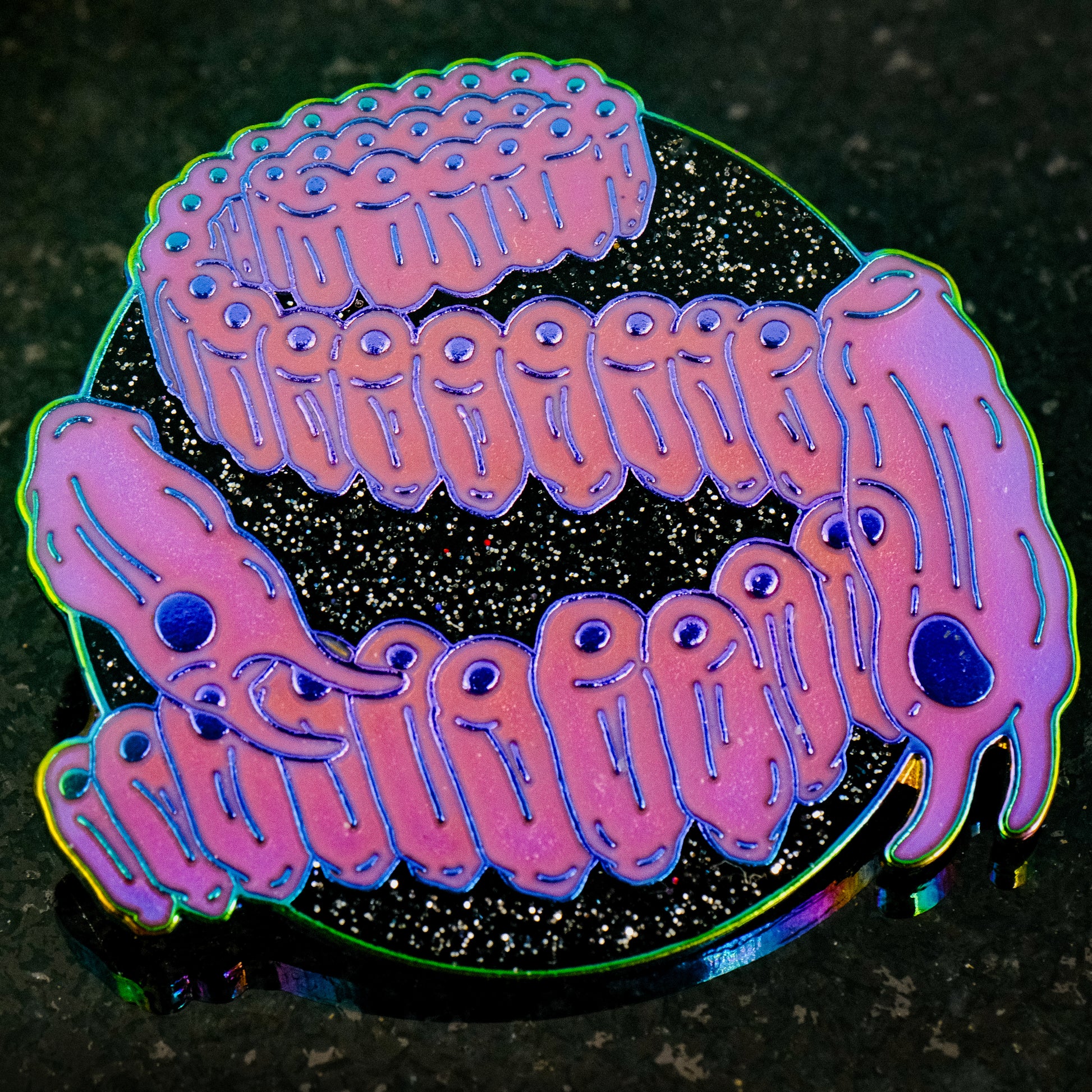 A photo of a soft enamel pin featuring Salps on a glittery black background with iridescent metal and bright magenta enamel. Rare