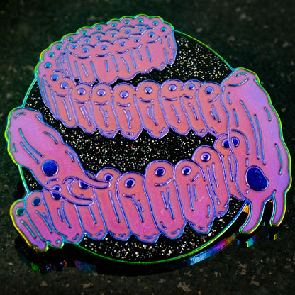 A photo of a soft enamel pin featuring Salps on a glittery black background with iridescent metal and bright magenta enamel. Rare